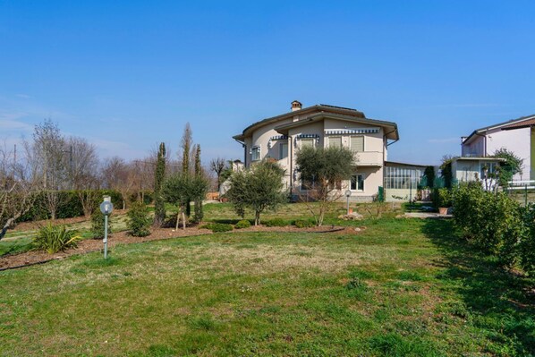 Une maison à deux étages, dotée d’un toit plat, entourée d’une pelouse bien entretenue et de quelques arbres.