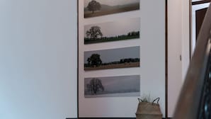 Un couloir orné de quatre tableaux représentant des paysages, un panier en osier posé sur une table et un cadre de porte en bois.
