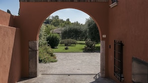 Une entrée en arc donne accès à un bâtiment, et une allée pavée mène à une pelouse verdoyante et à des arbres.
