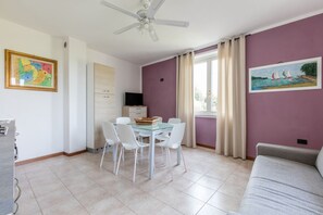 Ein Zimmer mit Esstisch, Stühlen, Deckenventilator, Sofa und zwei Bildern an den Wänden.