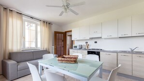 A modern kitchen with white cabinets, a dining area with a glass table, and a grey sofa. - GARDASUN 2 - Lovely flat Lake close Pet friendly (Padenghe Sul Garda)