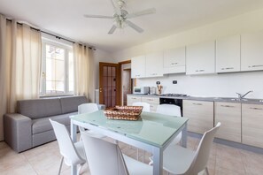 A modern kitchen with white cabinets, a dining area with a glass table, and a grey sofa. - GARDASUN 2 - Lovely flat Lake close Pet friendly (Padenghe Sul Garda)