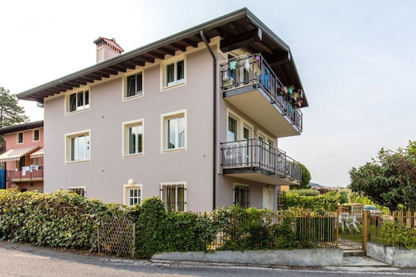 Ein mehrstöckiges Wohngebäude mit einem Balkon im oberen Geschoss, umgeben von viel Grün.