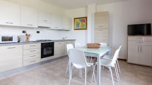 A modern kitchen with white cabinets, a dining table with chairs, a TV, and a ceiling fan. - GARDASUN 2 - Lovely flat Lake close Pet friendly (Padenghe Sul Garda)