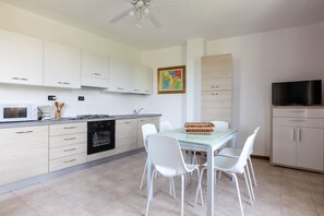 A modern kitchen with white cabinets, a dining table with chairs, a TV, and a ceiling fan.