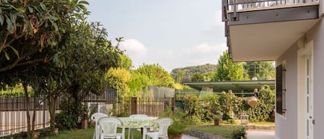 A patio with a table and chairs, surrounded by greenery and a fence.