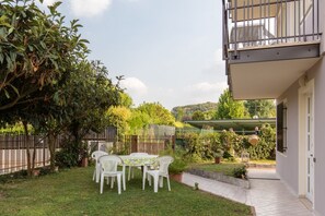 A patio with a table and chairs, surrounded by greenery and a fence.