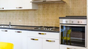 Een moderne keuken met witte kasten, een gasfornuis, een oven en een gele stoel.
