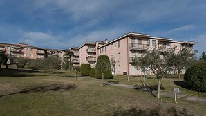 A row of pink apartment buildings with balconies, surrounded by well-maintained grass and trees. - Natural Chic - ON THE BEACH ON FOOT (Desenzano del Garda)