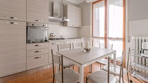 A modern kitchen with white cabinetry, a central island, and a dining area with a table and chairs. - Natural Chic - ON THE BEACH ON FOOT (Desenzano del Garda)