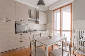 Una cocina moderna con armarios blancos, una isla central y un comedor con mesa y sillas.