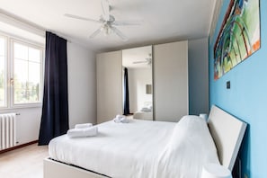 Habitación de hotel moderna con una cama grande, ventilador de techo, ventana con cortinas y un cuadro en la pared.