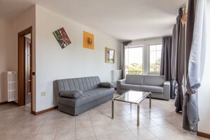 Una sala con dos sofás grises, una mesa de centro de vidrio y un radiador.