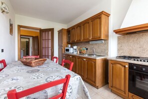 A kitchen with wooden cabinets, a microwave, a stove, and a dining table with red chairs.