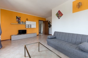 Un salón con un sofá gris, un mueble de entretenimiento blanco y una televisión.