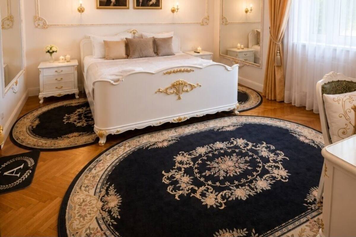 A bedroom with a large bed, a chandelier, two wall-mounted lamps, a mirror, and a window with curtains.