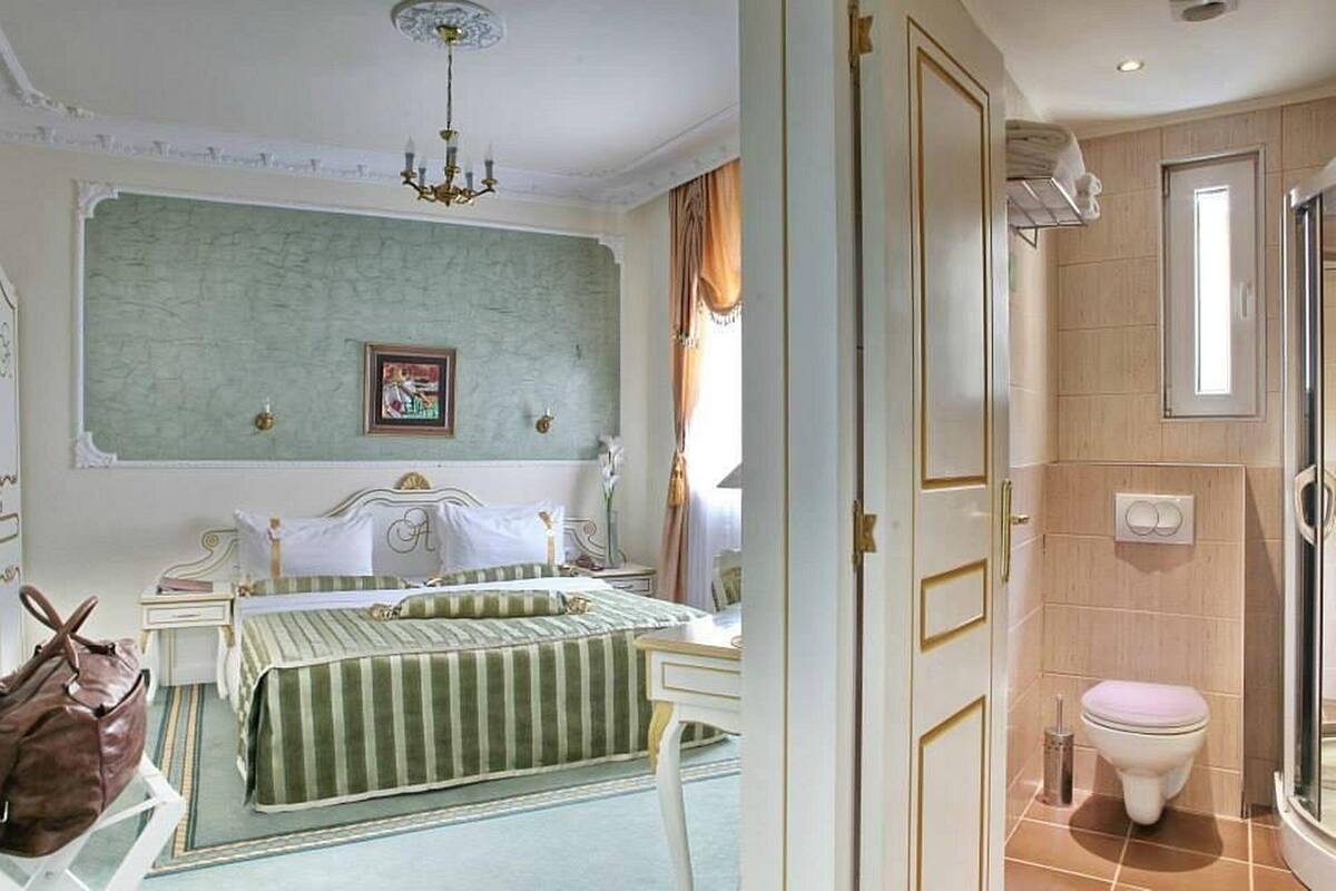A bedroom with a bed, bedside table, and a nightstand. There is a bathroom with a toilet and a shower.