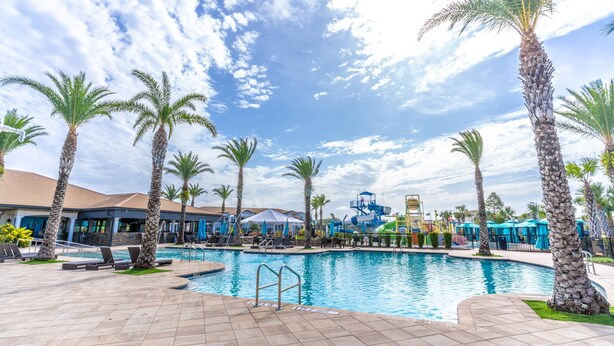 A swimming pool area with palm trees, lounge chairs, and a water slide. - 185 Balmoral (Haines City)