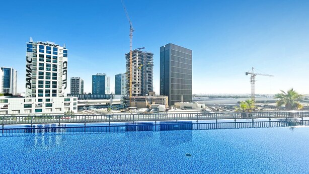 Un hôtel moderne doté d’une piscine, entouré de gratte-ciel et de grues de construction.
