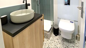 Ein modernes Badezimmer mit freistehender Waschtisch, einer Duschkabine aus Glas und einer Toilette.