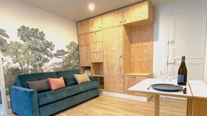 Ein Zimmer mit einem blauen Sofa, Holzschränken, einer weißen Tür und einem Tisch mit einer Weinflasche und Gläsern.