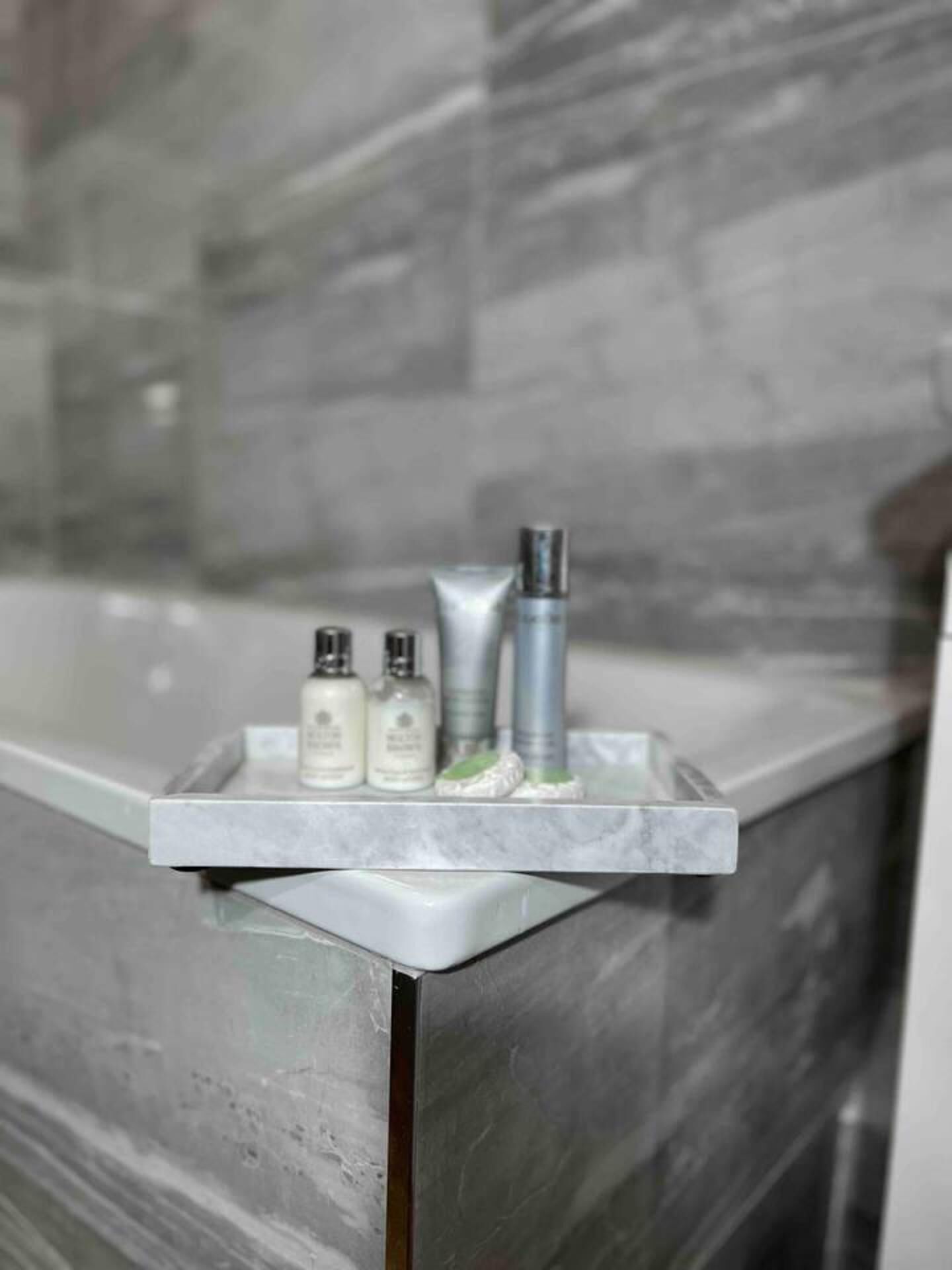 A bathroom with a marble countertop and a tray holding three toiletries.