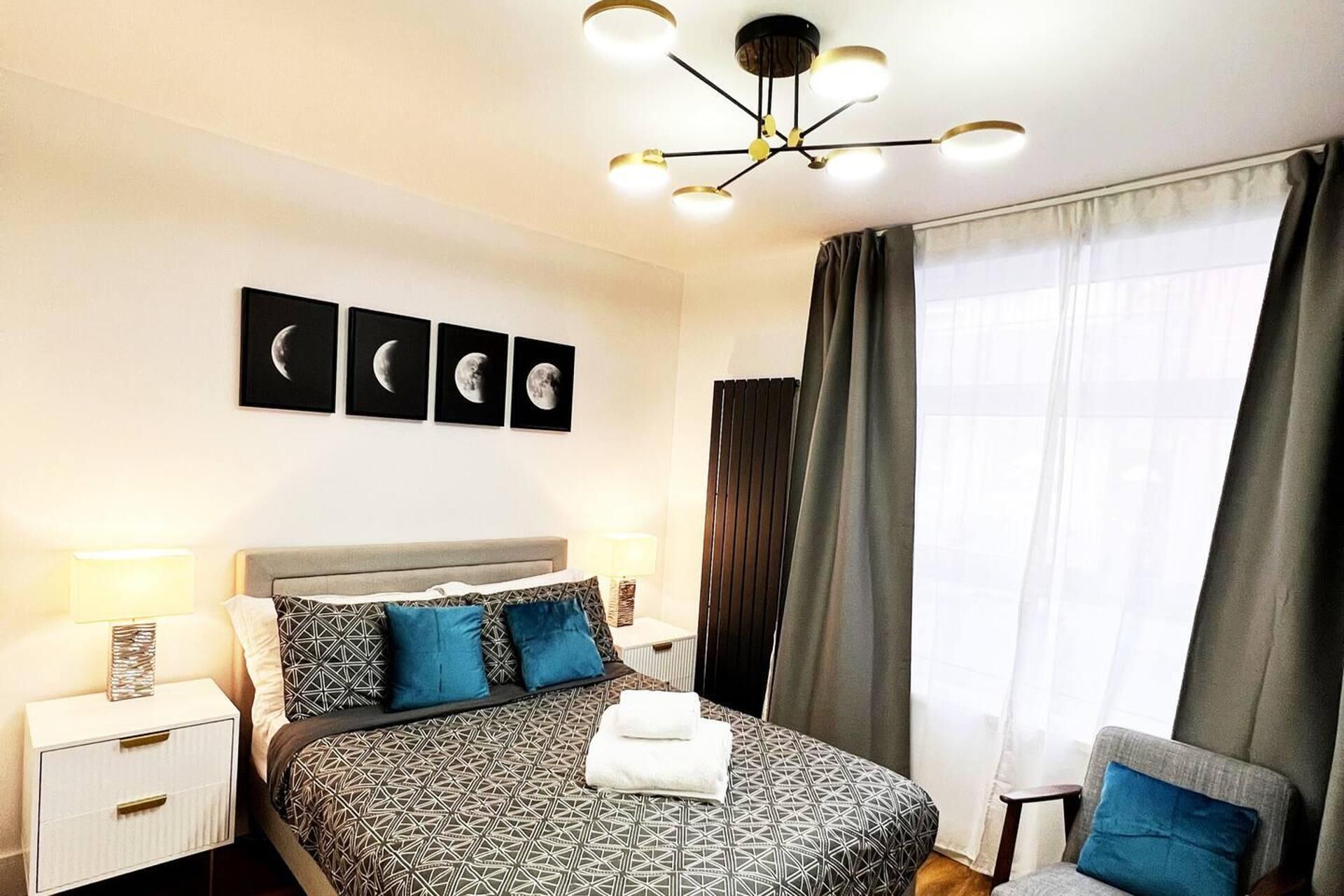 A hotel room with a bed, a nightstand, a chair, a window with curtains, and a ceiling light fixture.