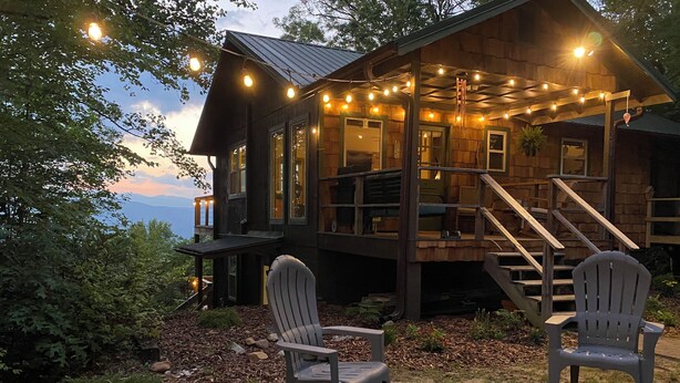 Eine Holzhütte mit einer Terrasse, zwei Adirondack-Stühlen und einer Feuerstelle.