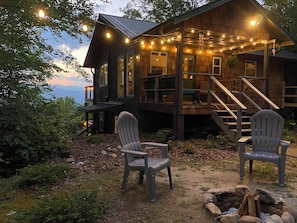 Eine Holzhütte mit einer Terrasse, zwei Adirondack-Stühlen und einer Feuerstelle.