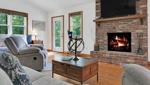 Ein Wohnzimmer mit Kamin, einer Couch, einem Couchtisch und einem Fernseher, der über dem Kamin angebracht ist.