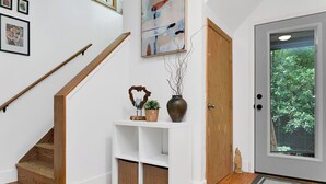 Eine Treppe mit Holzhandläufen, ein weißer Konsolentisch mit Dekoration und eine Tür mit Glasfenster sowie eine Fußmatte.