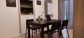 A small dining area with a table, four chairs, a laptop, a potted plant, and a cabinet.