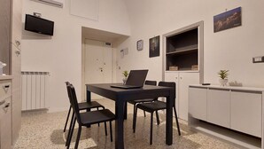 Cocina compacta con mesa, sillas, televisor, armarios y una planta pequeña.