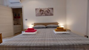 Una cama bien hecha con ropa de cama a rayas, dos mesitas de noche con lámparas y un cuadro sobre la cama.