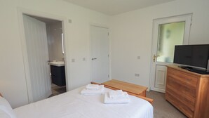 Un dormitorio con cama, cómoda de madera, televisor y baño visible a través de una puerta abierta.