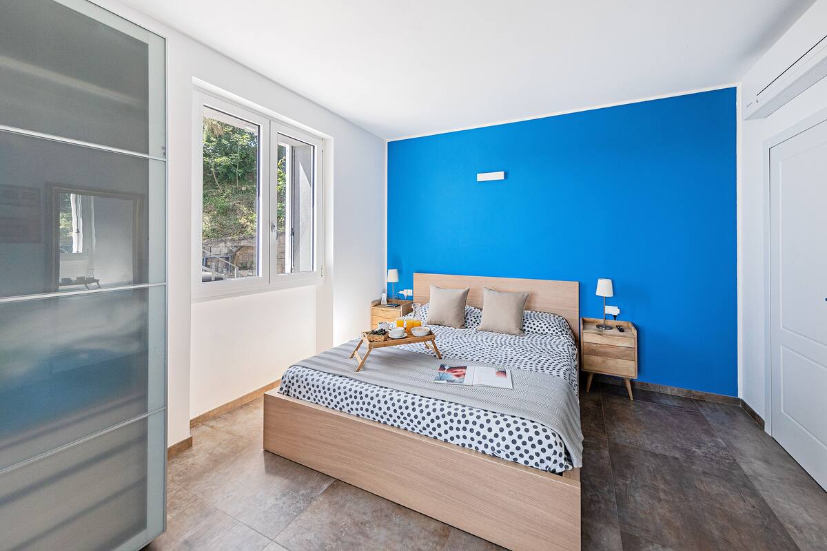 A modern bedroom with a large bed, a bedside table, a nightstand, and a window.