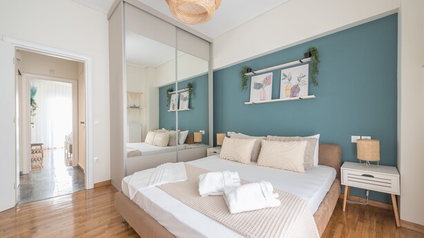 A modern bedroom with a large bed, a bedside table, a mirror, and a wall with framed artwork. - The Luxury Suite by Cloudkeys (Athens)