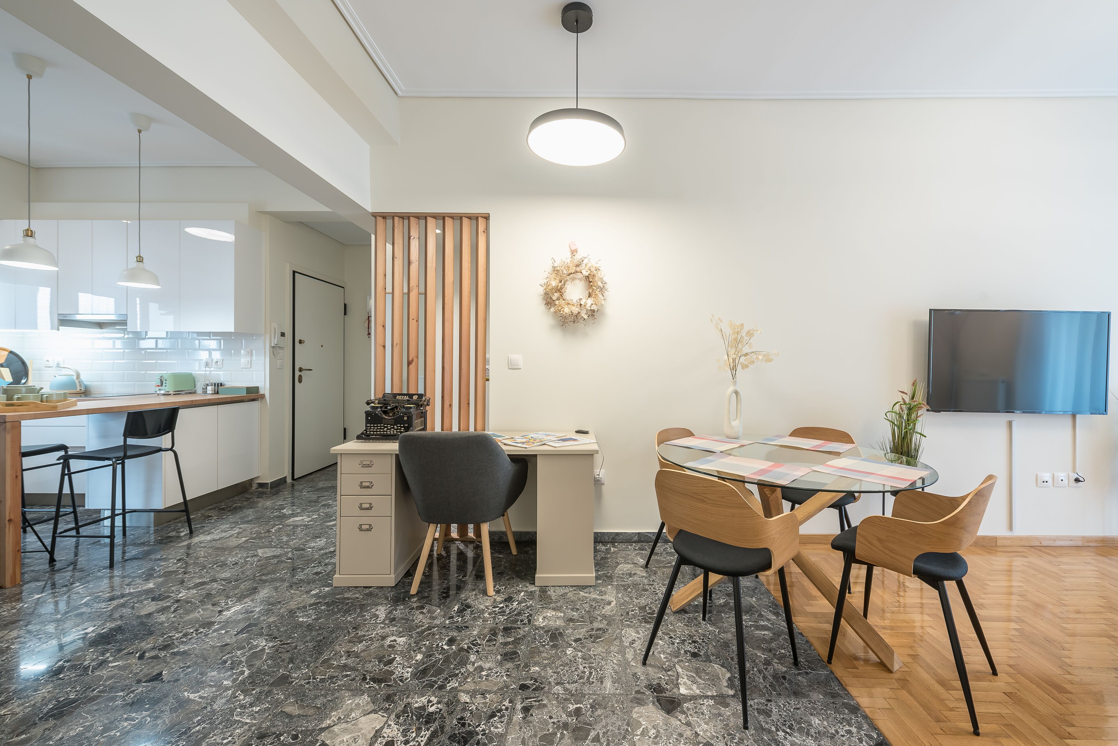 Una cocina moderna con zona de comedor, que presenta suelo de mármol, mobiliario de madera y un televisor de pantalla plana.