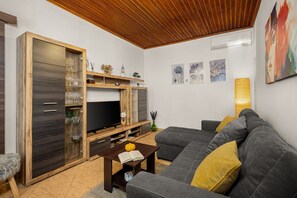 Ein Wohnzimmer mit Sofa, Fernseher, Holzschrank und Kunstwerk an der Wand.