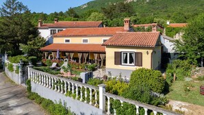 Eine Villa an einem Hang mit Terrakotta-Dächern, einer überdachten Terrasse und einer Steinmauer.
