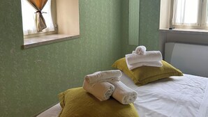 Une chambre d’hôtel avec deux lits, des murs verts, une télévision, une fenêtre avec des rideaux et un miroir.