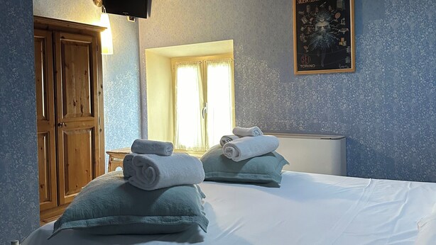 Une chambre avec un plafond en bois, un lit recouvert de draps blancs, deux oreillers, une table de chevet, un téléviseur et une affiche accrochée au mur.