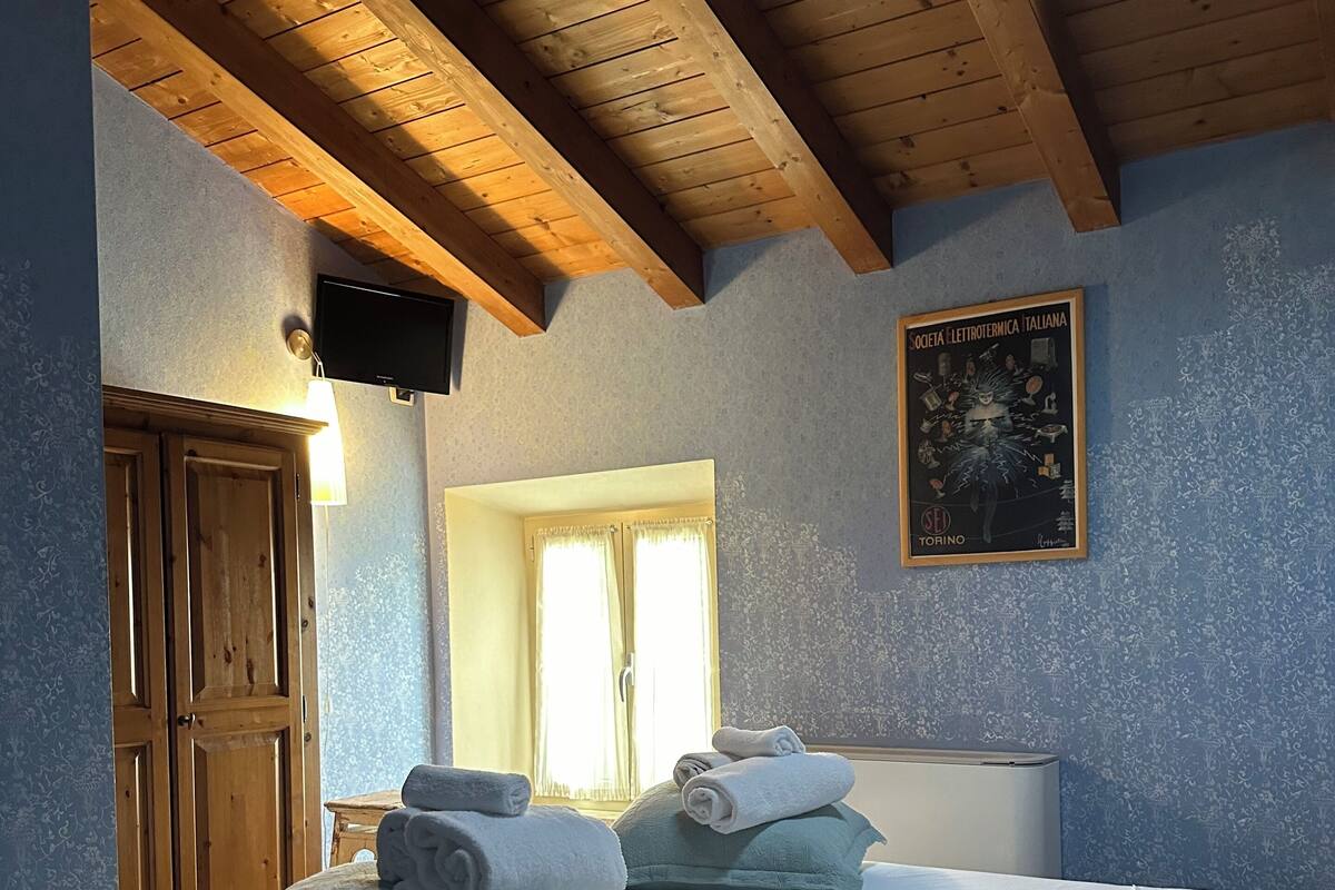 Ein Schlafzimmer mit Holzboden, einem Bett mit weißen Leinen, zwei Kissen, einem Nachttisch, einem Fernseher und einem Poster an der Wand.