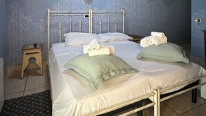 Une chambre à coucher avec un lit en métal, deux oreillers, une petite table de chevet et une commode.
