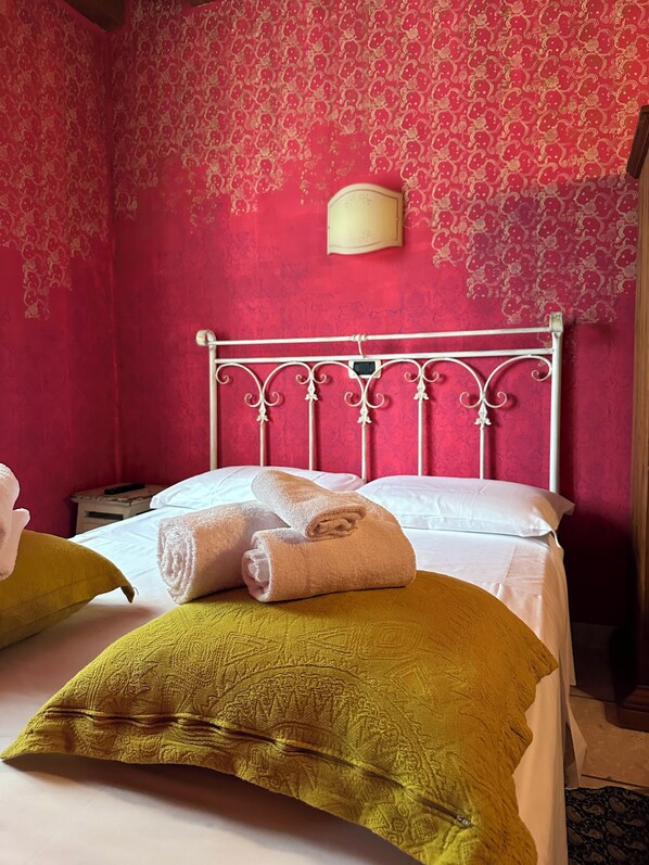 Quarto com cama, duas almofadas, mesa de cabeceira e luminária fixada na parede.