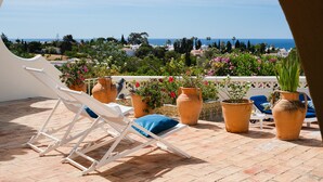 Eine Terrasse mit einer weißen Liege, Topfpflanzen und Blick aufs Meer.