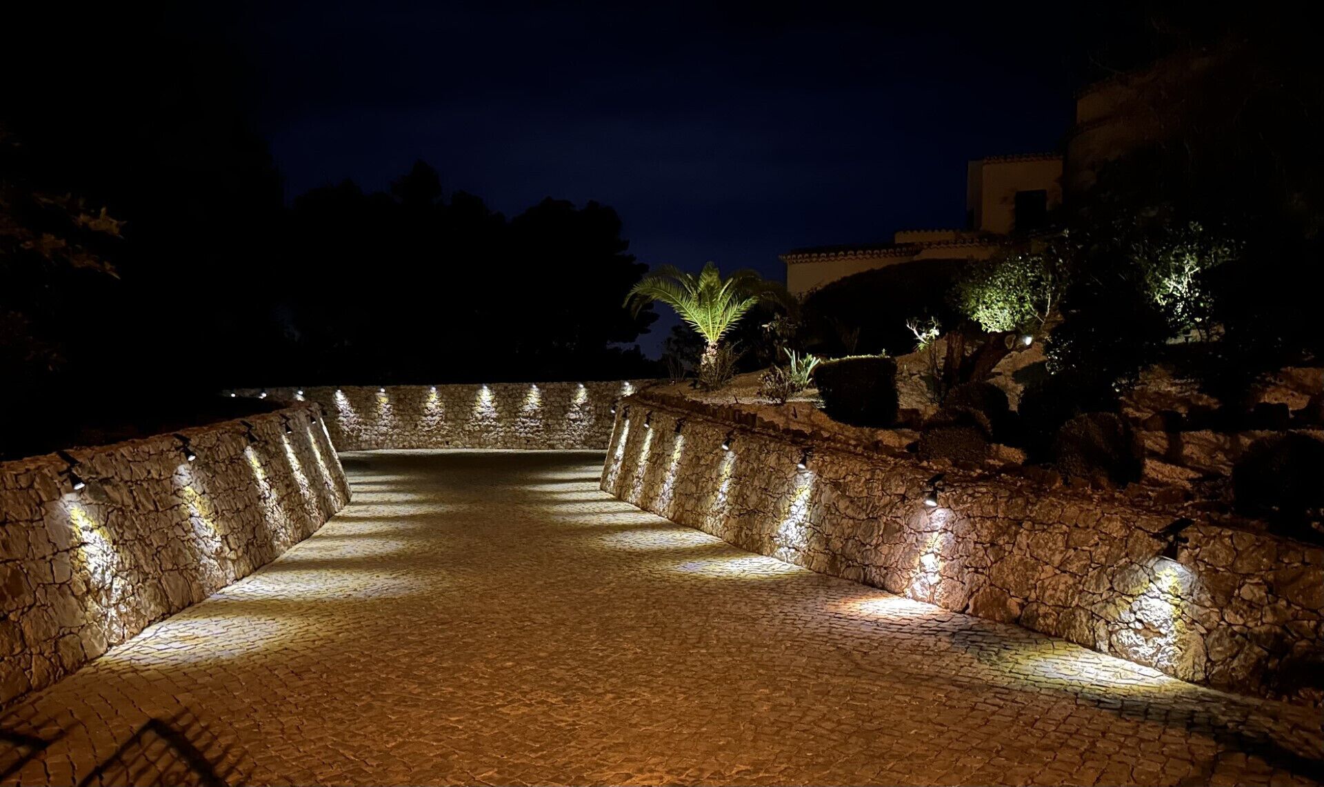 Uma trilha de pedra leva a um edifício à noite, iluminado por luzes.