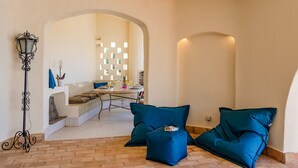 Ein Zimmer mit Fliesenboden, einer Couch mit Kissen, einem Tisch mit Gegenständen und einer Wand mit geometrischem Muster.