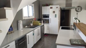A modern kitchen with white cabinetry, a built-in microwave, and a dishwasher. There is a window above the sink and a clock on the wall. - Quiet house in Provence (Saint-Cannat)