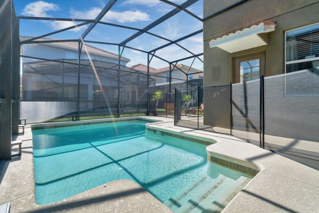 Une piscine dotée d’une enceinte en verre, entourée d’une terrasse avec des marches menant à une porte.